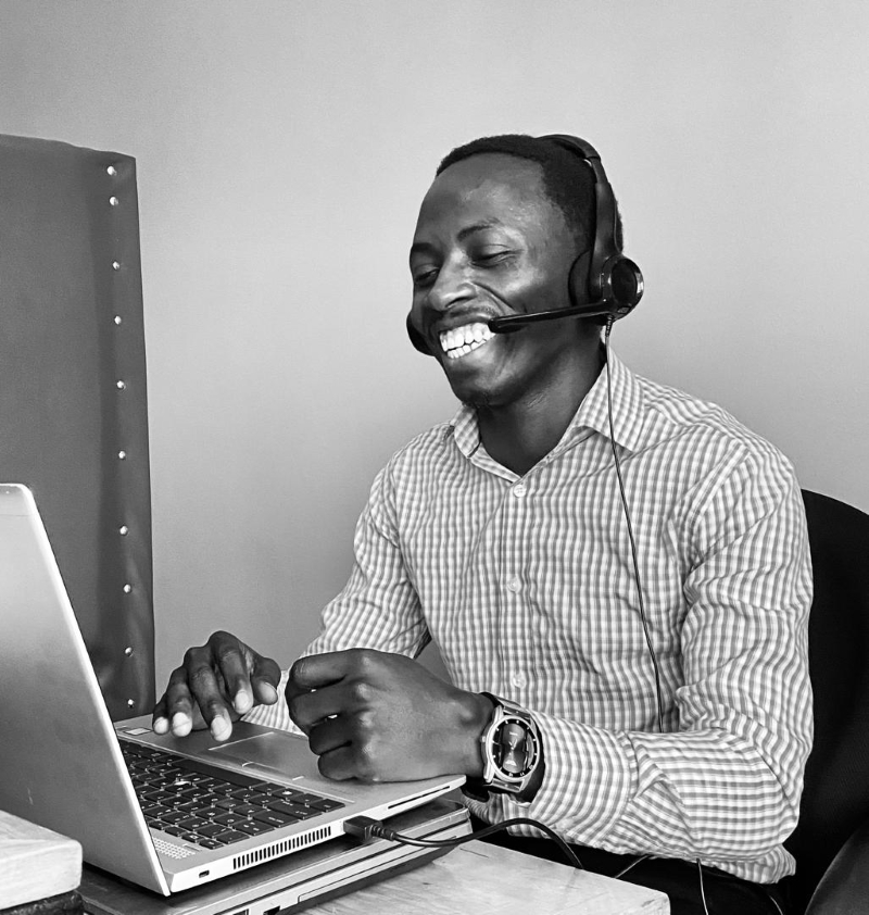 Samuel is sat with his headset on at his desk with his laptop smiling